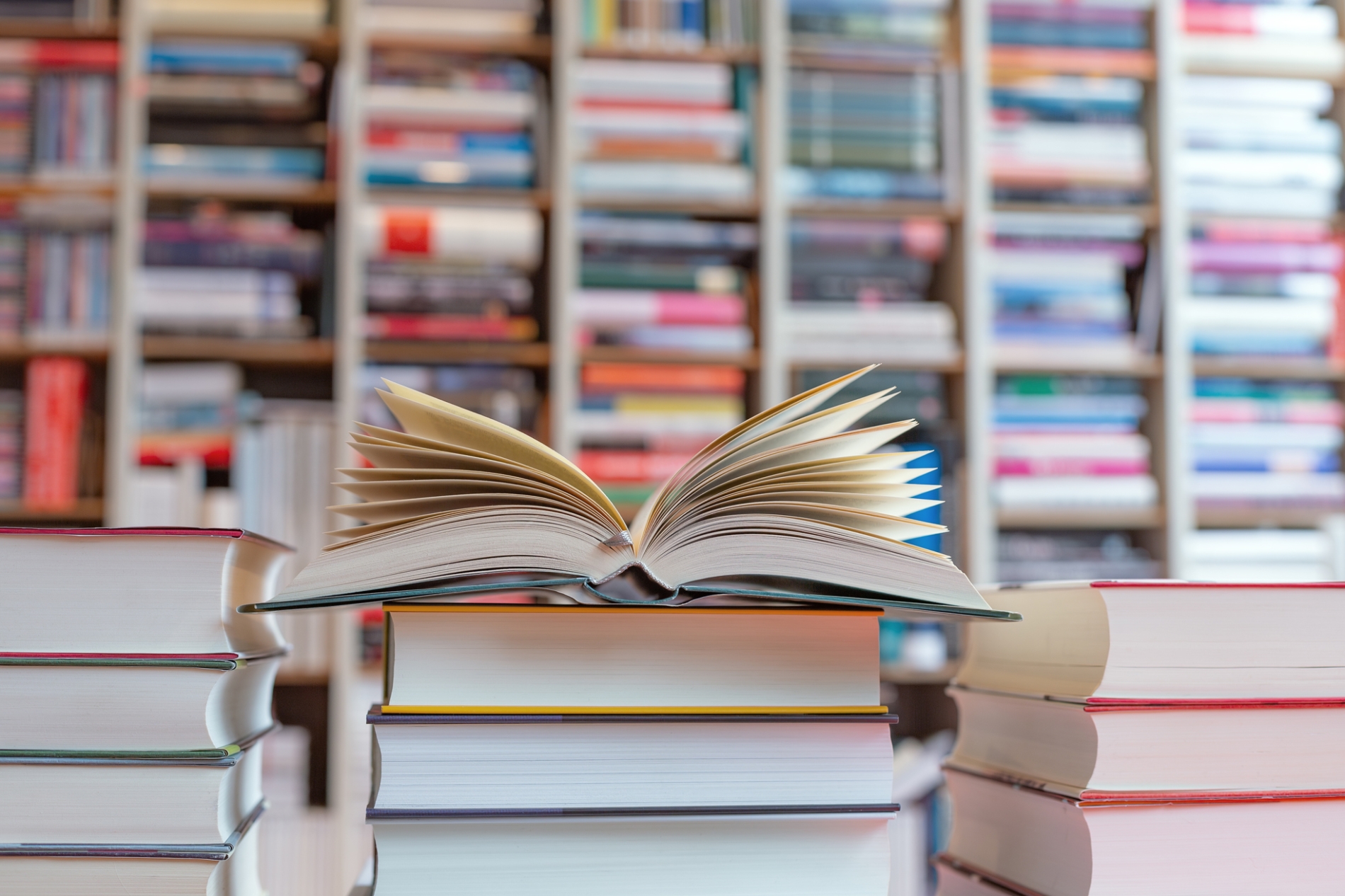 Open,Novel,On,Stack,Of,Books,In,Front,Of,Shelf